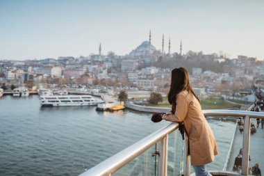 asian woman leaning on a bridge looking at panoramic view of beautiful city of instanbul and bosphorus in turkey