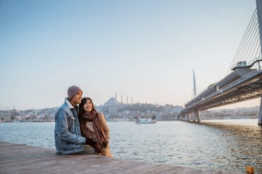 young couple relaxing on the side of bosphorus during sunset. beautiful woman and man with istanbul city scape at the background