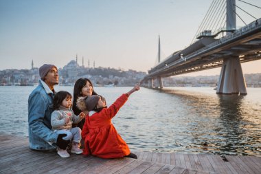 happy asian family sitting on the side of bosphorus looking at beautiful sunset in istanbul turkey