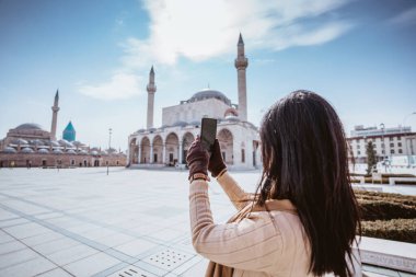 portrait of a woman taking picture of beautiful mosque and mevlana museum in konya turkey