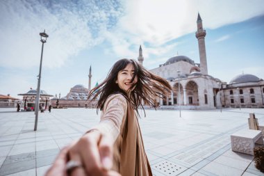 attractive woman holding hand and taking someone to get closer with mosque in the background