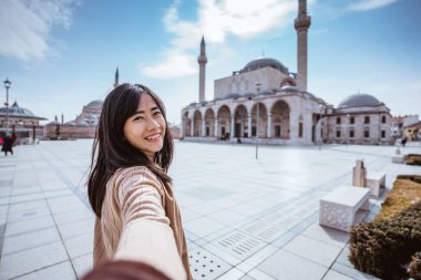 attractive woman holding hand and taking someone to get closer with mosque in the background