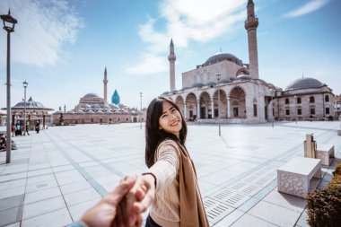 attractive woman holding hand and taking someone to get closer with mosque in the background