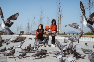portrait of happy mother and daughter enjoy feeding pigeon in city square