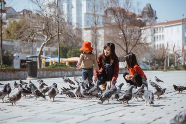 portrait of happy mother and daughter enjoy feeding pigeon in city square