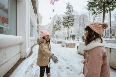 two little girl fighting snow ball in the city during winter