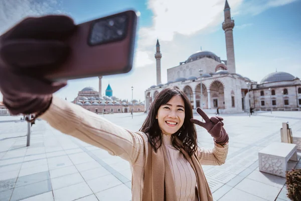 beautiful asian woman taking selfie portrait in front of the mosque in konya turkey