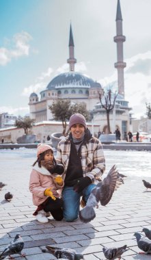 father and daughter feeding the bird together in taksim square turkey