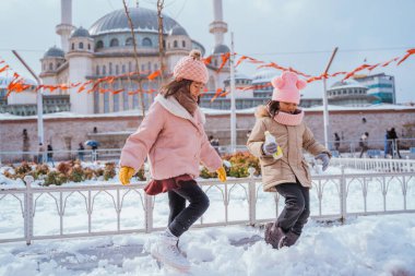 two little girl playing with snow in city square with the mosque in the background