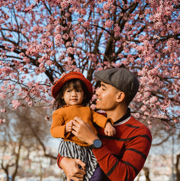 happy father and daughter looking at cherry blossom in the park