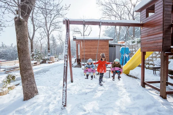 Girl Help Swinging Her Brother Sister Playing Snowy Playground — 스톡 사진