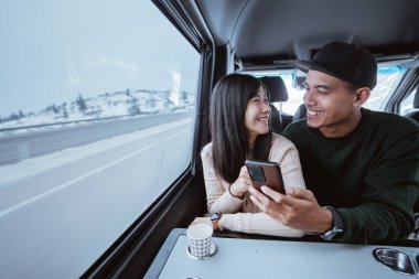 asian couple using smartphone together while traveling by car sitting by the window