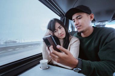 serious couple while looking at mobile phone during their journey on a car or van