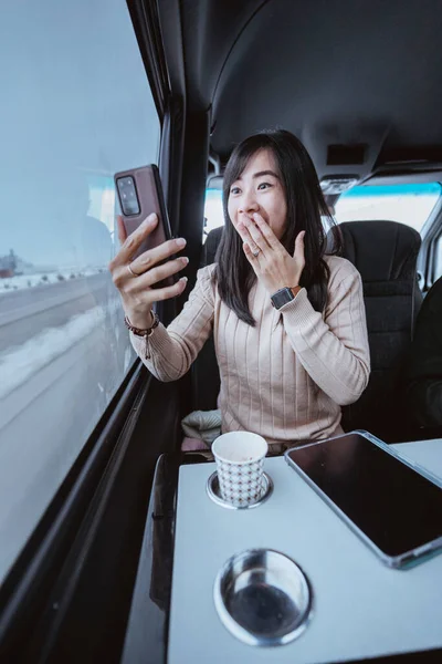 suprised young woman cover her mouth while looking at her mobile phone screen inside a moving car