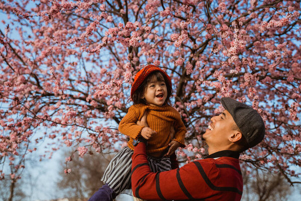 happy father and daughter looking at cherry blossom in the park