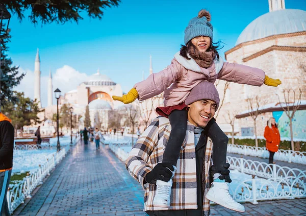 father carrying her daughter in his shoulder while visiting hagia sophia mosque in winter holiday