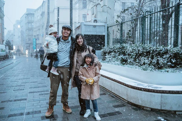 portrait of asian family wearing warm clothing standing in the middle of snow fall in winter. family travel in turkey