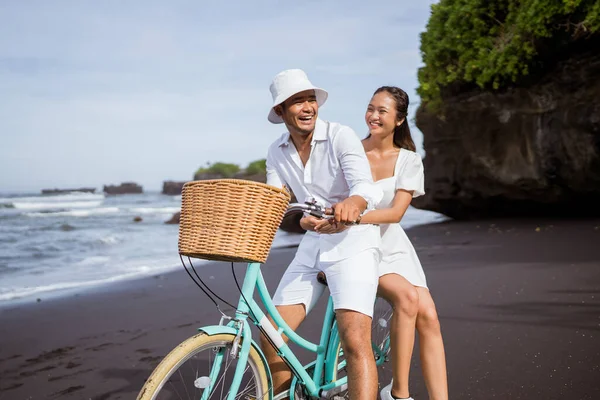 The happy couple with bikes sit on the bike together at the beach