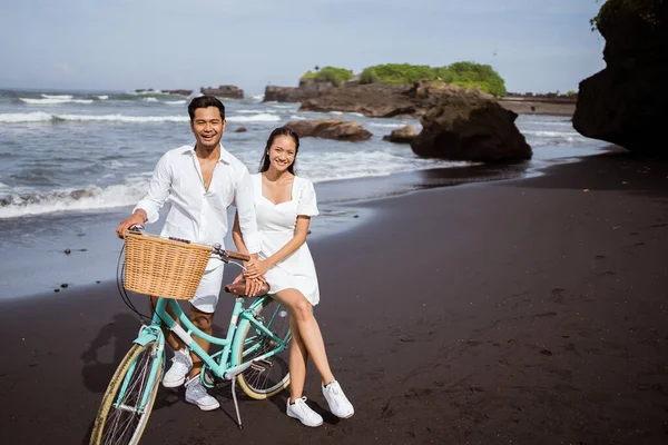 The happy couple with bikes sit on the bike together at the beach