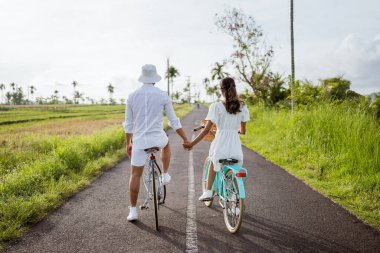 beautiful couple holding hand while riding a bicycle on the road in the countryside. shooting from behind