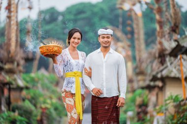 smiling balinese couple carrying an holy offering during galungan day in penglipuran village bali clipart