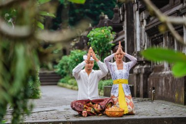 balinese hindu couple put their hand on top of their head while doing the prayer at pura in the morning clipart