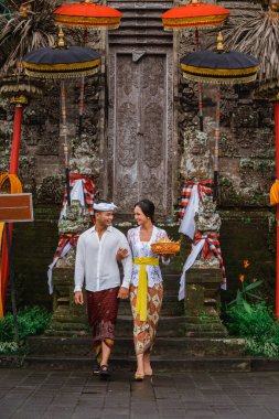 couple with balinese traditional clothing walking in front of pura gate