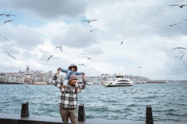 father carrying daughter on his shoulder enjoying the view of bosphorus straits with so many seagulls flying around