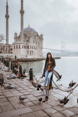 beautiful woman sitting near bosphorus with ortakoy mosque at the background