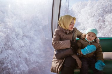 potrait of a muslim woman and kid riding a cable car in the beautiful snowy mountain in turkey