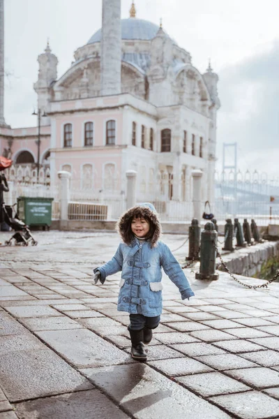 happy kid running around the square in turkey with ortakoy mosque in the background