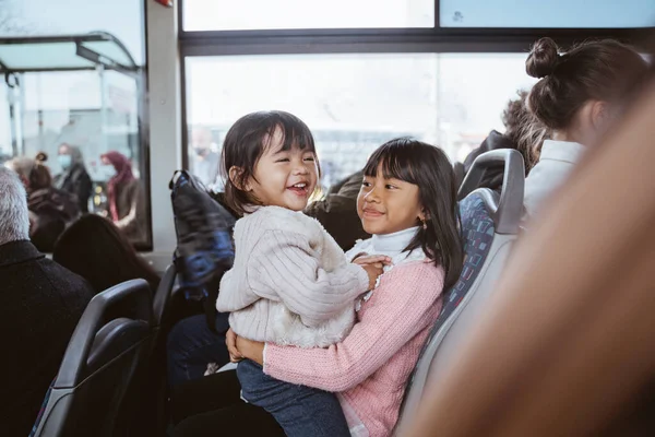lovely asian little girl sitting on her older sisters lap while riding public bus together