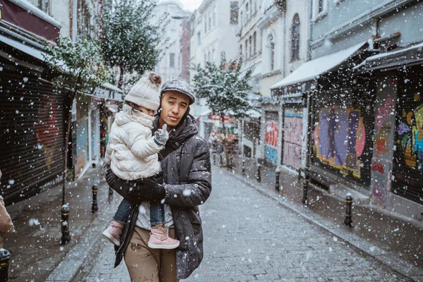 portrait of father carrying his daughter during snow fall in the city