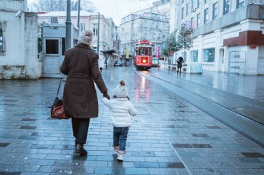 portrait of a mother holding her toddler hand and walk together during winter shoot from behind