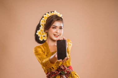 beautiful asian balinese woman with kebaya showing her mobile phone screen to camera