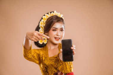 beautiful asian balinese woman with kebaya showing her mobile phone screen to camera