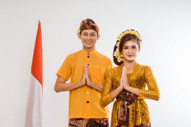 balinese couple with greeting gesture to camera. woman and man wearing traditional balinese costume over isolated background
