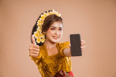 beautiful asian balinese woman with kebaya showing her mobile phone screen to camera with thumb up gesture