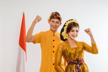 excited balinese couple put hands up looking at camera over brown background