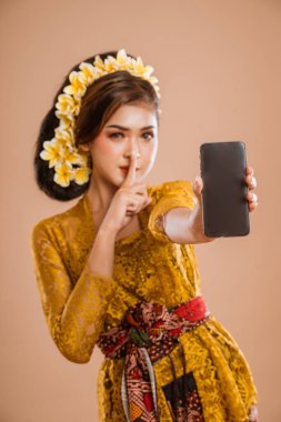 balinese woman with kebaya showing her mobile phone screen to camera with silent gesture