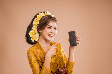 beautiful asian balinese woman with kebaya showing her mobile phone screen to camera