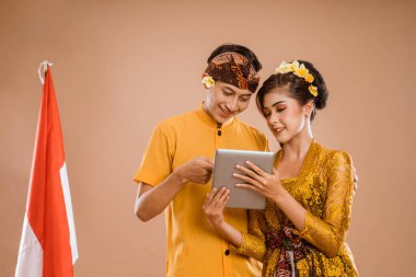 man and woman wearing balinese traditional clothing using tablet pc and smiling