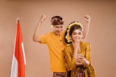 excited young balinese couple while using mobile phone over isolated background