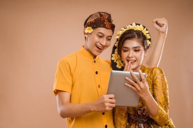 excited balinese couple using tablet pc together over isolated background