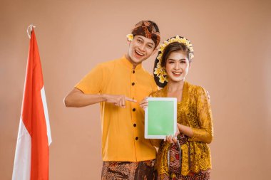 balinese young couple showing tablet screen to camera. man and woman asian wearing kebaya and traditional cloth from bali