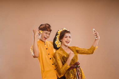 excited young balinese couple while using mobile phone over isolated background