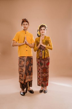 balinese couple with greeting gesture to camera. woman and man wearing traditional balinese costume over isolated background