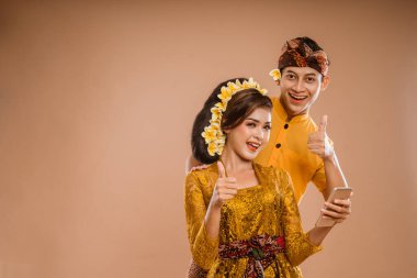 excited young balinese couple while using mobile phone over isolated background