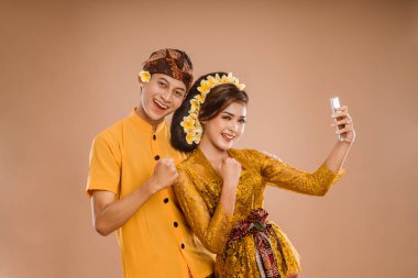 excited young balinese couple while using mobile phone over isolated background