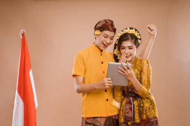 excited balinese couple using tablet pc together over isolated background